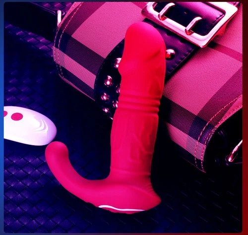 Bright red retractable vibration toy with white tip, black strap, and Bluetooth-enabled white device on black-white plaid bag.